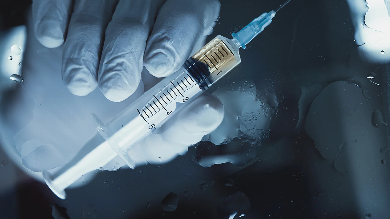 close up of syringe with liquid in gloved hand