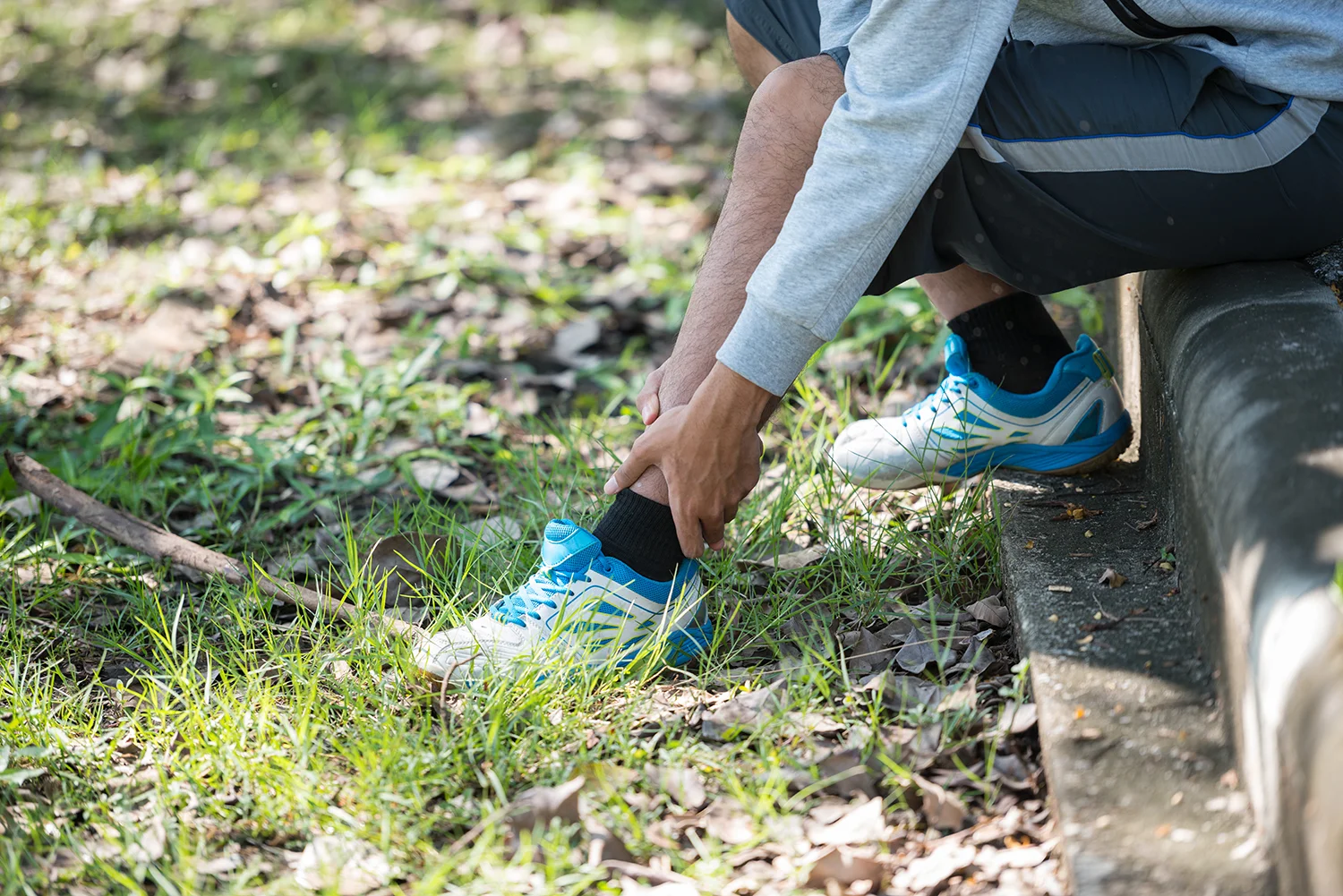 man touching ankle while sitting outside on grass